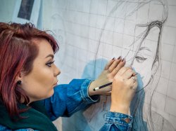 Student drawing a portrait with pencil on large graph paper on wall at the College of the Arts.